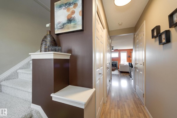 Interior hallway with beige walls, wood-look floor, and doors. Stairs on left. - 2879 23 St Nw, Edmonton