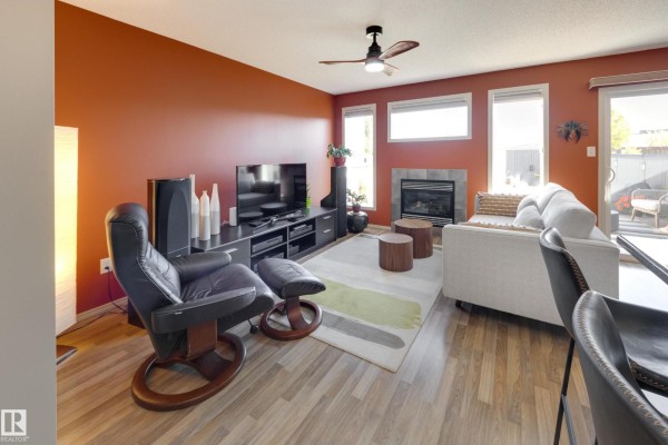 Living room with orange walls, fireplace, sofa, recliner, and sliding glass door. - 2879 23 St Nw, Edmonton