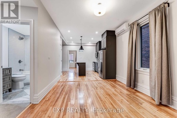 Living area with hardwood floors, air conditioning unit, and view into the kitchen and bathroom. - 288 Arlington Avenue, Ottawa
