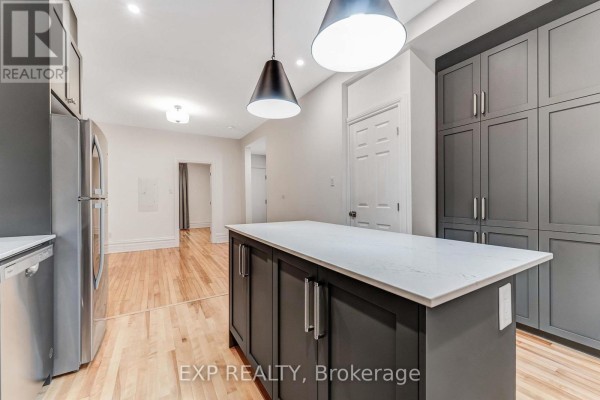 Kitchen island with white quartz countertop facing a wall of grey pantry cabinets and appliances. - 288 Arlington Avenue, Ottawa