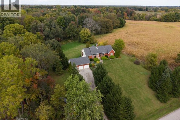 Drone shot of a residential property with a red brick house and an attached garage, nestled amongst mature trees. - 288 Thirteenth Concession Road, Scotland