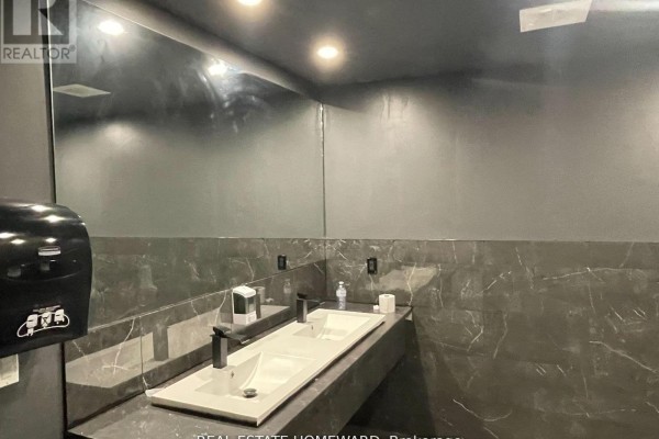 Commercial washroom with a double sink, black faucets, and large grey marble-look mirrors. - 2880b Kingston Road, Toronto