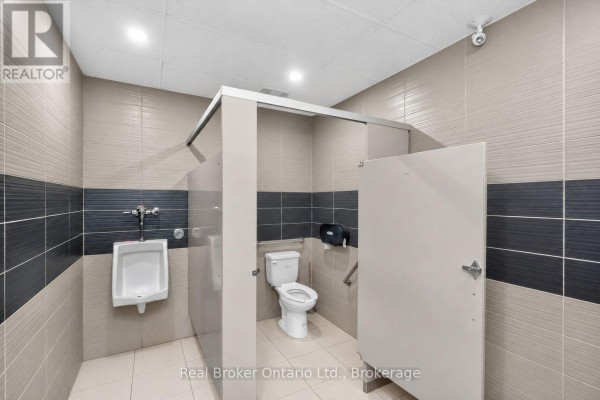 Commercial washroom with urinals, toilet stalls, and tiled walls. - 289 King Street, Midland