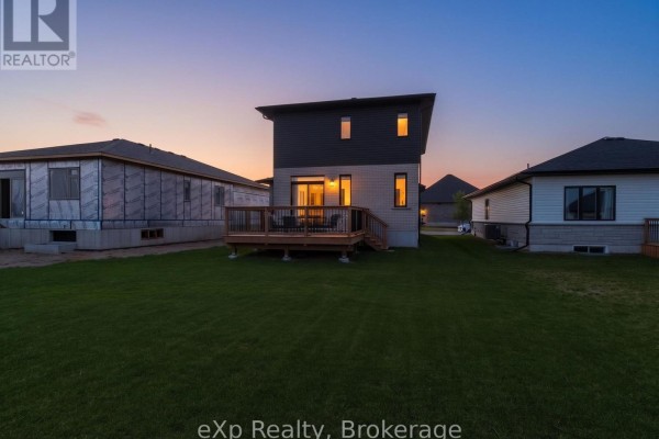 Rear exterior of a house with a dark grey and white facade, a wooden deck, and grass. - 289 Mary Rose Avenue, Saugeen Shores
