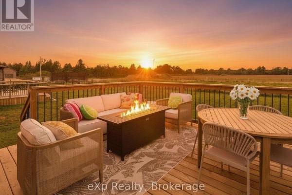Wooden deck with outdoor furniture, a fire pit, and a table set against a sunset sky. - 289 Mary Rose Avenue, Saugeen Shores