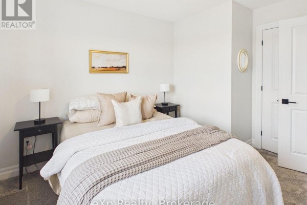 Bedroom with a queen bed, white bedding, a black nightstand, and a white textured wall. - 289 Mary Rose Avenue, Saugeen Shores
