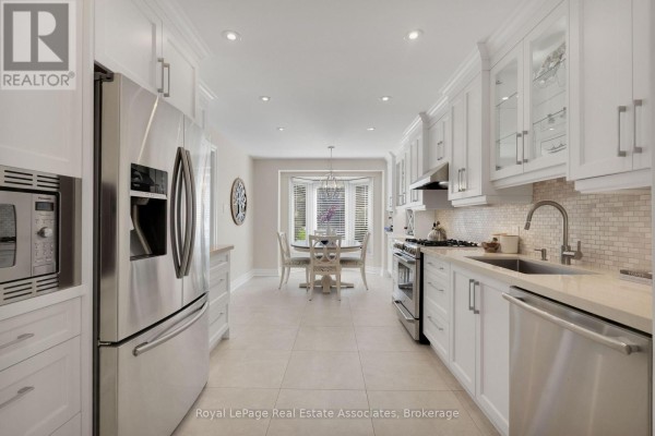 Long white kitchen with stainless steel appliances, stone countertops, and a view of a breakfast nook. - 29 - 3265 South Millway, Mississauga