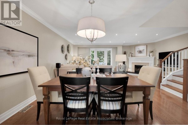 Dining room with a wooden table, upholstered chairs, fireplace, and staircase with wooden railings. - 29 - 3265 South Millway, Mississauga