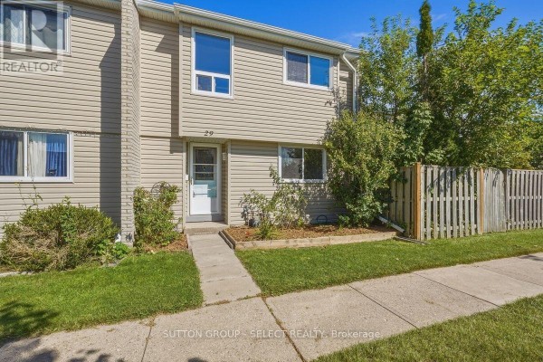 Exterior view of a beige vinyl-sided townhouse with a concrete walkway and green lawn. - 29 - 669 Osgoode Drive, London South