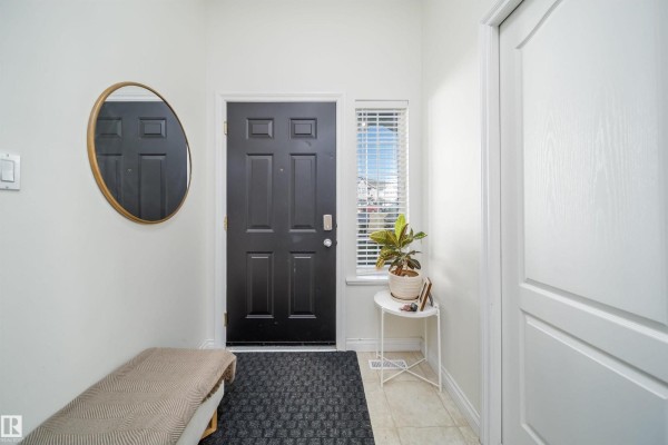 Interior entryway with a black front door, beige bench, round mirror, and potted plant. - #29 200 Erin Ridge Dr, St  Albert