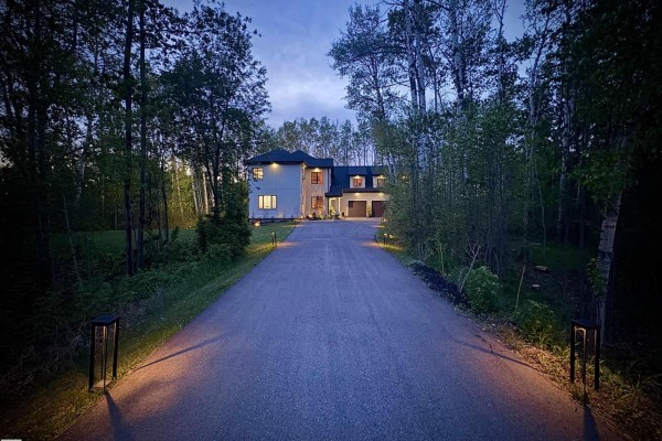 Exterior view of a large stucco house with multiple windows and illuminated garage doors. - #29 26516 Twp Road 514 Sw Sw, Rural Parkland County