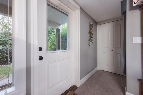 View from inside looking out a glass-paned front door towards a covered porch and greenery. - 29 45025 Wolfe Road, Chilliwack Proper West, Chilliwack