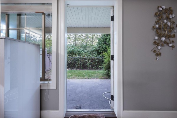 View through an open back door showing a fenced backyard with a paved patio and trees. - 29 45025 Wolfe Road, Chilliwack Proper West, Chilliwack