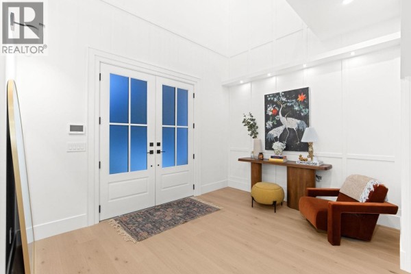 Entryway with white double doors, console table, artwork, and an orange armchair. - 29 50 Street, Delta
