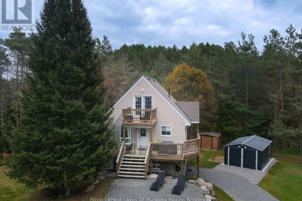 Aerial view of a beige house surrounded by mature trees, featuring decks and a gravel driveway. - 29 Amylee Drive, Perry