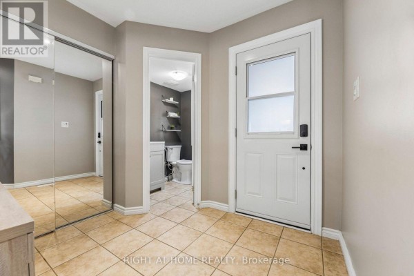 Interior hallway with tiled floors, mirrored closet doors, and a doorway to a powder room. - 29 Bannister Street, Clarington