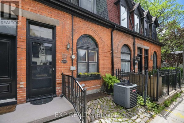 Close-up of a brick townhouse exterior with a black door, arched window, and air conditioning unit. - 29 Belmont Street, Toronto