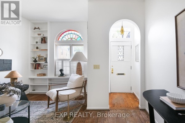 View of a living room with built-in white bookshelves, a stained-glass window, and an arched doorway. - 29 Belmont Street, Toronto