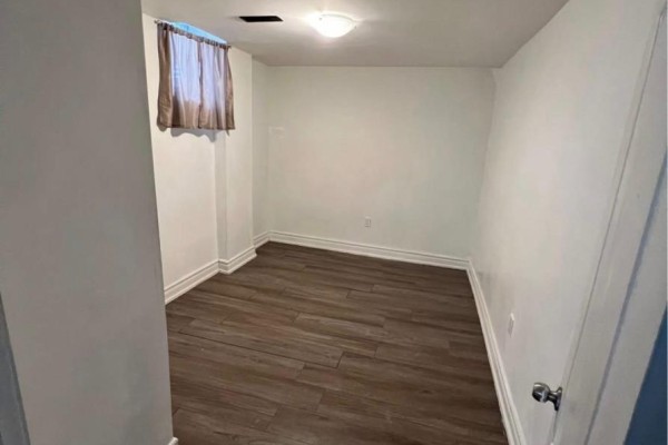 An empty room with wood-look flooring and a small window with brown curtains. - 29 Brightly Drive, Ajax