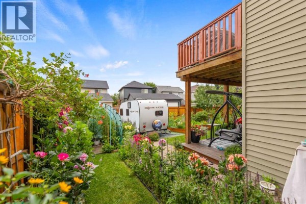 Backyard view with a small Rove Lite trailer, greenhouse, and flower beds. - 29 Brightoncrest Heights Se, Calgary