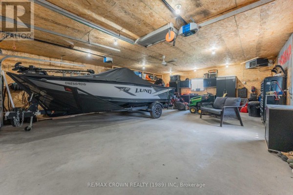 Interior of a spacious garage with a covered Lund boat, lawnmower, and seating area. - 29 Hazel Street, Kapuskasing