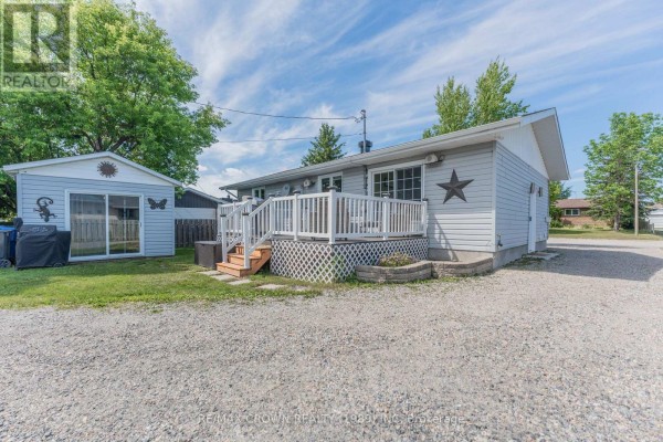 Rear exterior of a grey house with a white wooden deck, a small shed, and a gravel driveway. - 29 Hazel Street, Kapuskasing