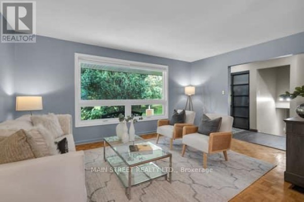 Living room with large window overlooking trees, two armchairs, and a glass coffee table. - 29 Johnston Street, Georgina