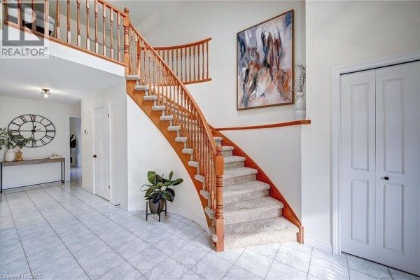 Foyer featuring a grand curved wooden staircase with carpeted steps and lofted landing. - 29 Napoleon Drive, Stoney Creek