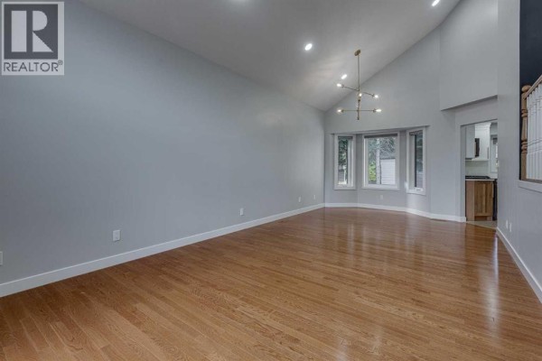 Living room with vaulted ceiling, hardwood floors, bay windows, and a modern chandelier. - 29 Pickwick Lane, Lacombe