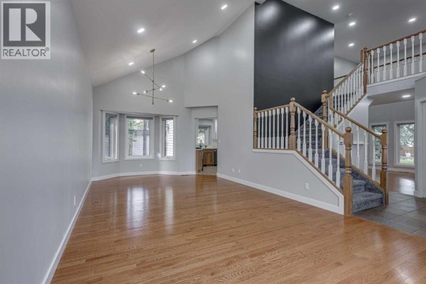 Living room with vaulted ceiling, hardwood floors, bay windows, and a prominent staircase. - 29 Pickwick Lane, Lacombe