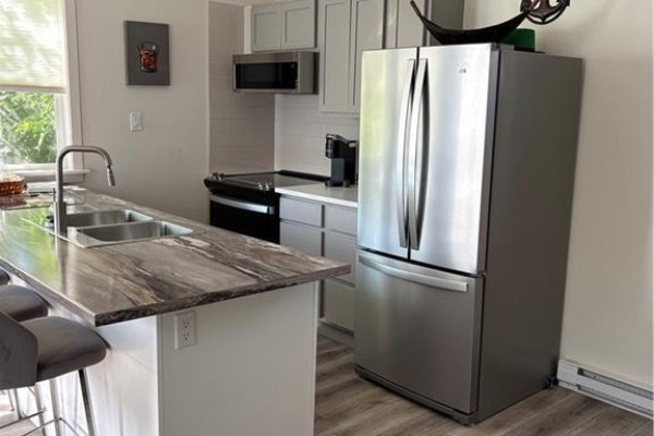 Open-concept living area with gray flooring and kitchen appliances visible - 29 Railway Avenue, Pointe Du Chene