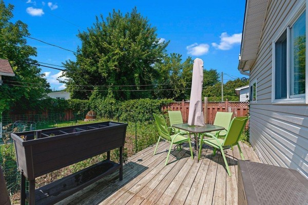 A wooden deck in the backyard with green chairs and a table, next to a raised planter. - 29 Rue Michaud, Gatineau