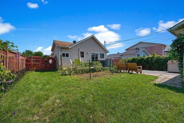 A view of the backyard showing a lawn, wooden fence, deck, and bench seating. - 29 Rue Michaud, Gatineau