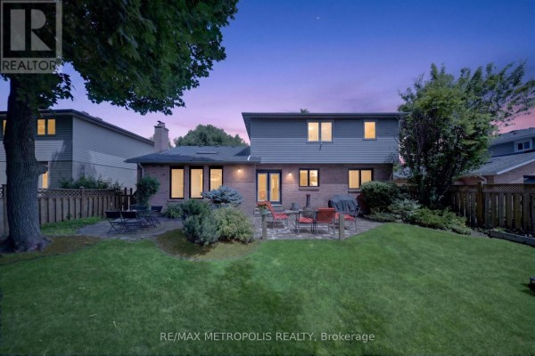 Backyard view of a two-story house with a brick patio, green lawn, and twilight sky. - 29 Winter Way, Brantford