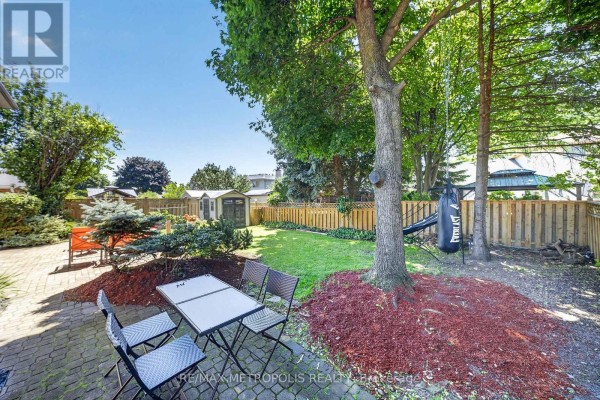 Backyard patio with a table and chairs, surrounded by grass, trees, and a wooden fence. - 29 Winter Way, Brantford