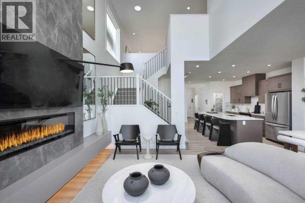 Living room fireplace with glass, two black chairs, and view of staircase and kitchen. - 29 Wolf Hollow Common Se, Calgary