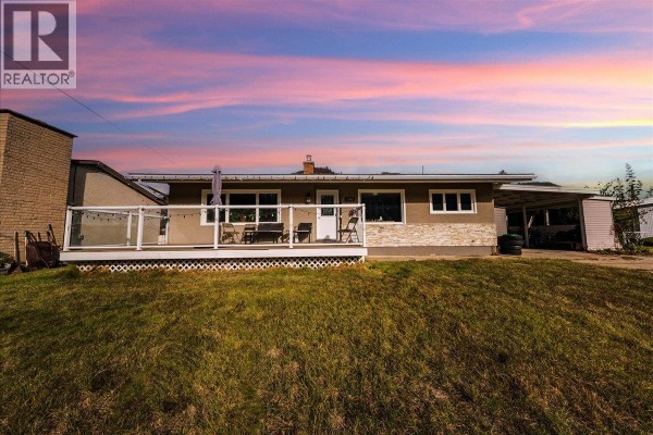 Rear view of the single-story house with a deck and adjacent carport under a colorful sunset sky. - 290 8th Avenue, Montrose