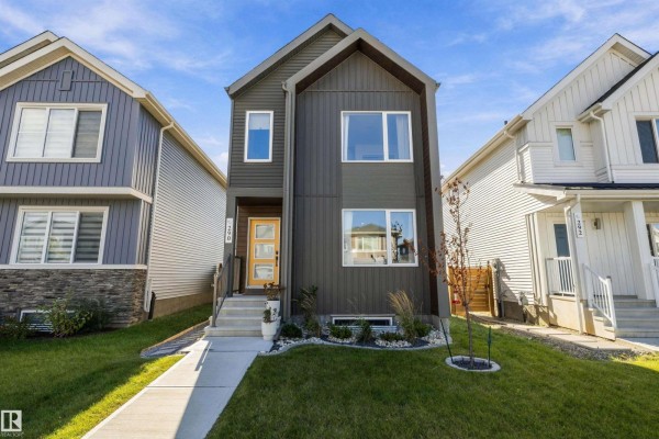 Front view of a modern home with dark gray siding, a wood-accented entrance, and large windows. - 290 Jensen Lakes Bv, St  Albert