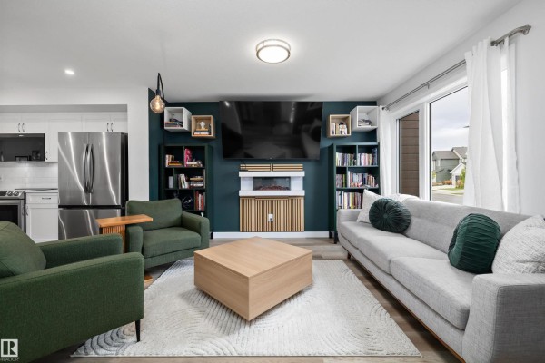 Living room with a gray sofa, green armchairs, built-in bookshelves, an electric fireplace, and a large window. - 290 Jensen Lakes Bv, St  Albert