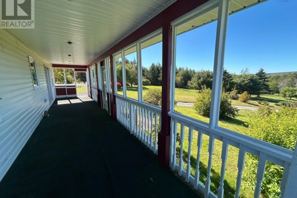 View from a covered porch with white railings and red trim, overlooking a green lawn and trees. - 290 Macvicar Road, Enon