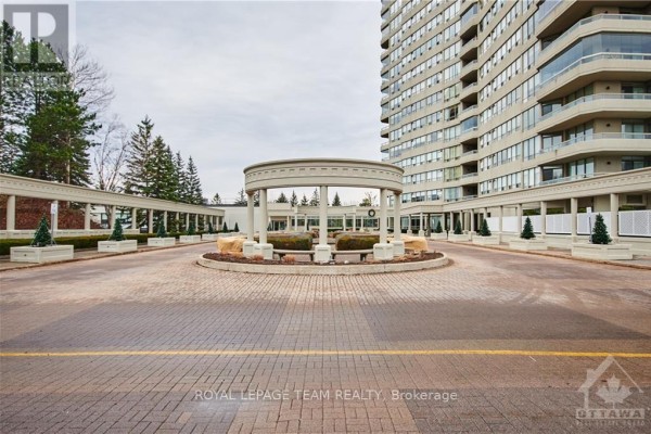 The circular driveway entrance to a tall apartment building with columns and decorative landscaping. - 2903 - 1480 Riverside Drive, Ottawa