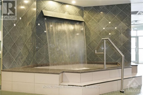 A built-in jacuzzi with a cascading waterfall feature and tiled walls, illuminated by overhead lights. - 2903 - 1480 Riverside Drive, Ottawa