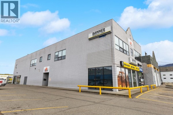 Commercial garage interior with a large roll-up door, yellow exit door, and stored boxes. - 2903 43 Avenue, Vernon