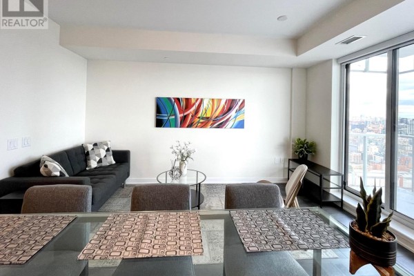 Living room with dark sofa, glass coffee table, and dining area in foreground. - 2908 - 28 Freeland Street, Toronto