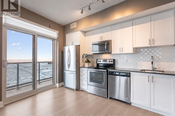 Kitchen with white cabinetry, stainless steel appliances, black countertops, and a sliding glass door to a balcony. - 2908 - 3600 Highway 7, Vaughan