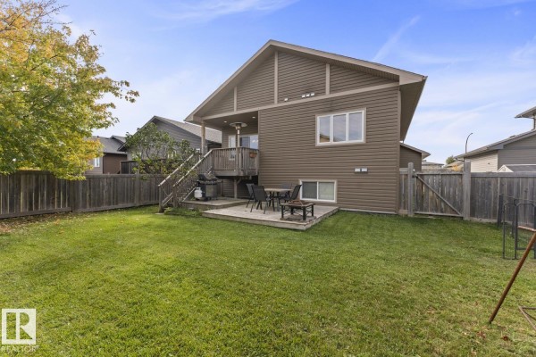 Rear exterior view of a beige house with a deck, backyard, and wooden fence. - 2908 Goldenrod Ga, Cold Lake