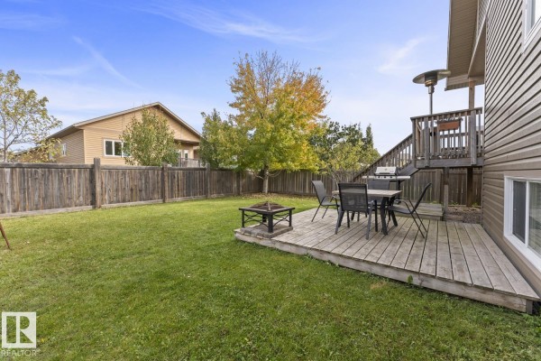 View of the backyard from the deck, showing a lawn, fence, and patio furniture. - 2908 Goldenrod Ga, Cold Lake