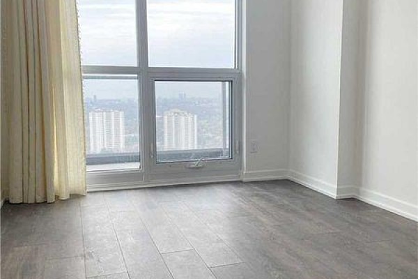 Empty room with large windows showing a cityscape and light beige curtains. - 2909 - 32 Forest Manor Street, Toronto