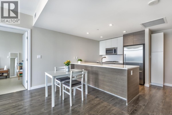 Open concept living area with large windows, a grey sofa, and a kitchen island with a sink. - 2909 4485 Skyline Drive, Burnaby
