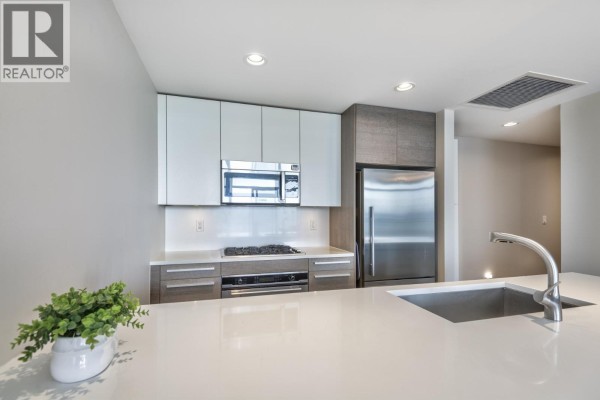 Kitchen island with quartz countertop and stainless steel sink, adjacent to white and grey cabinetry. - 2909 4485 Skyline Drive, Burnaby